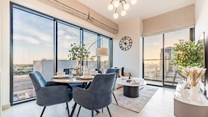 A modern living room with large windows, a dining area, and a view of the cityscape. - City Views 1BR Close to Golf Course & Attractions, Binghatti Venus, Jumeirah Village Circle (Dubai)