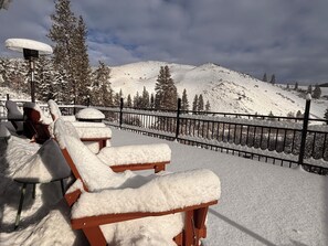Des fauteuils de jardin recouverts de neige, une clôture en métal et un paysage montagneux enneigé.