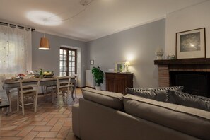 Una sala de estar con sofá, mesa de comedor, sillas, lámpara colgante, chimenea y ventana.