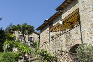 A stone building with a balcony, a staircase, and potted plants.