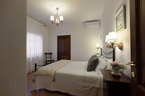 Un dormitorio con cama, mesita de noche, lámpara, silla, puerta y ventana con cortinas.