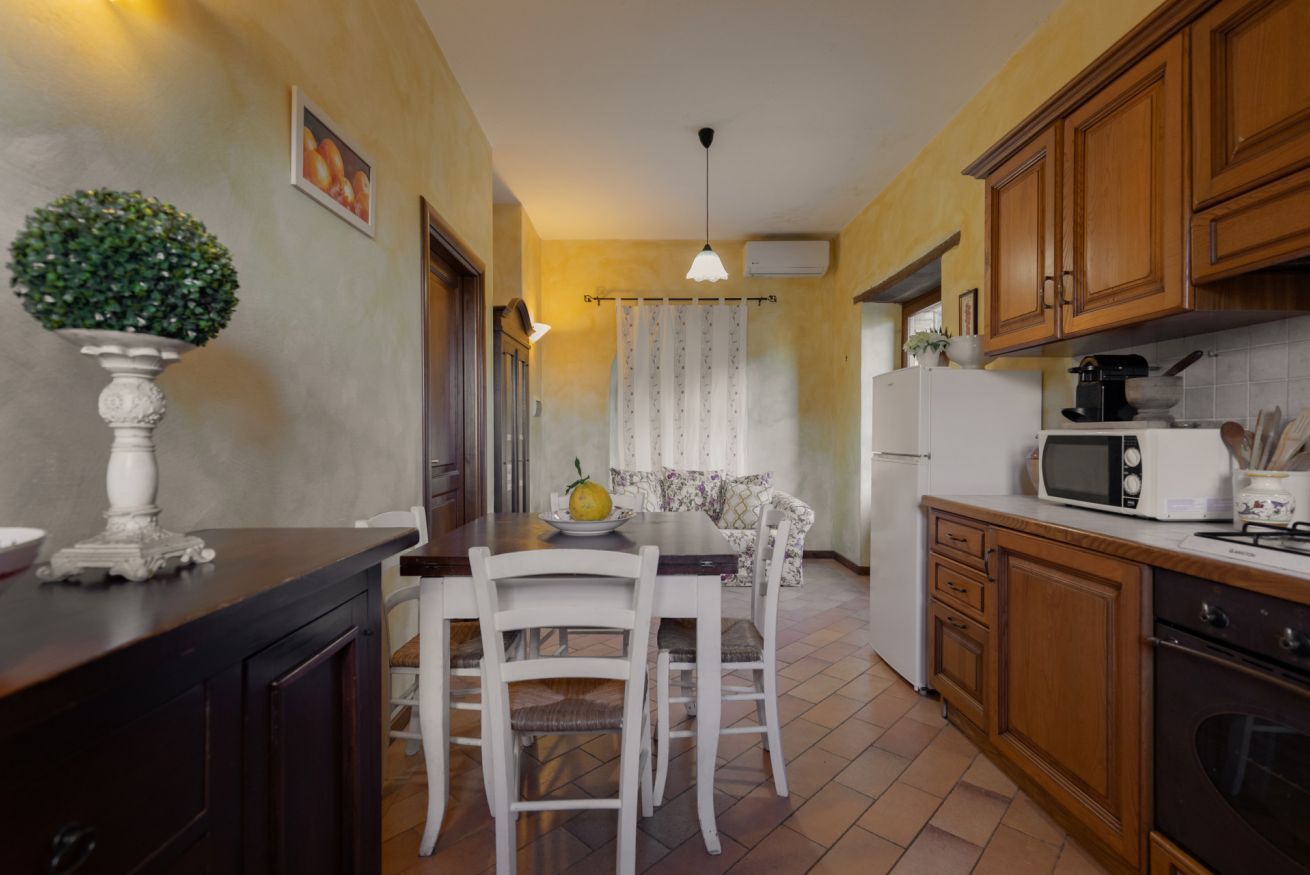 A compact kitchen with wooden cabinets, a dining table with chairs, a white refrigerator, and a microwave.