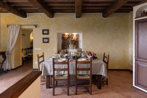 A dining room with a table set for four, wooden chairs, a chandelier, and a rustic wall decor.