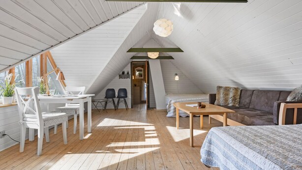 A cozy attic bedroom with a sloped ceiling, wooden flooring, a bed, a sofa, a dining table with chairs, and a desk with a chair. - Nice home in Farsø with WiFi (Farsø)