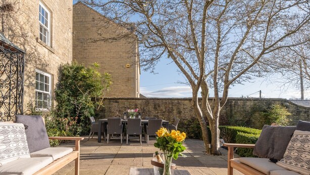 An outdoor patio with a stone table, wicker furniture, and a vase of flowers.