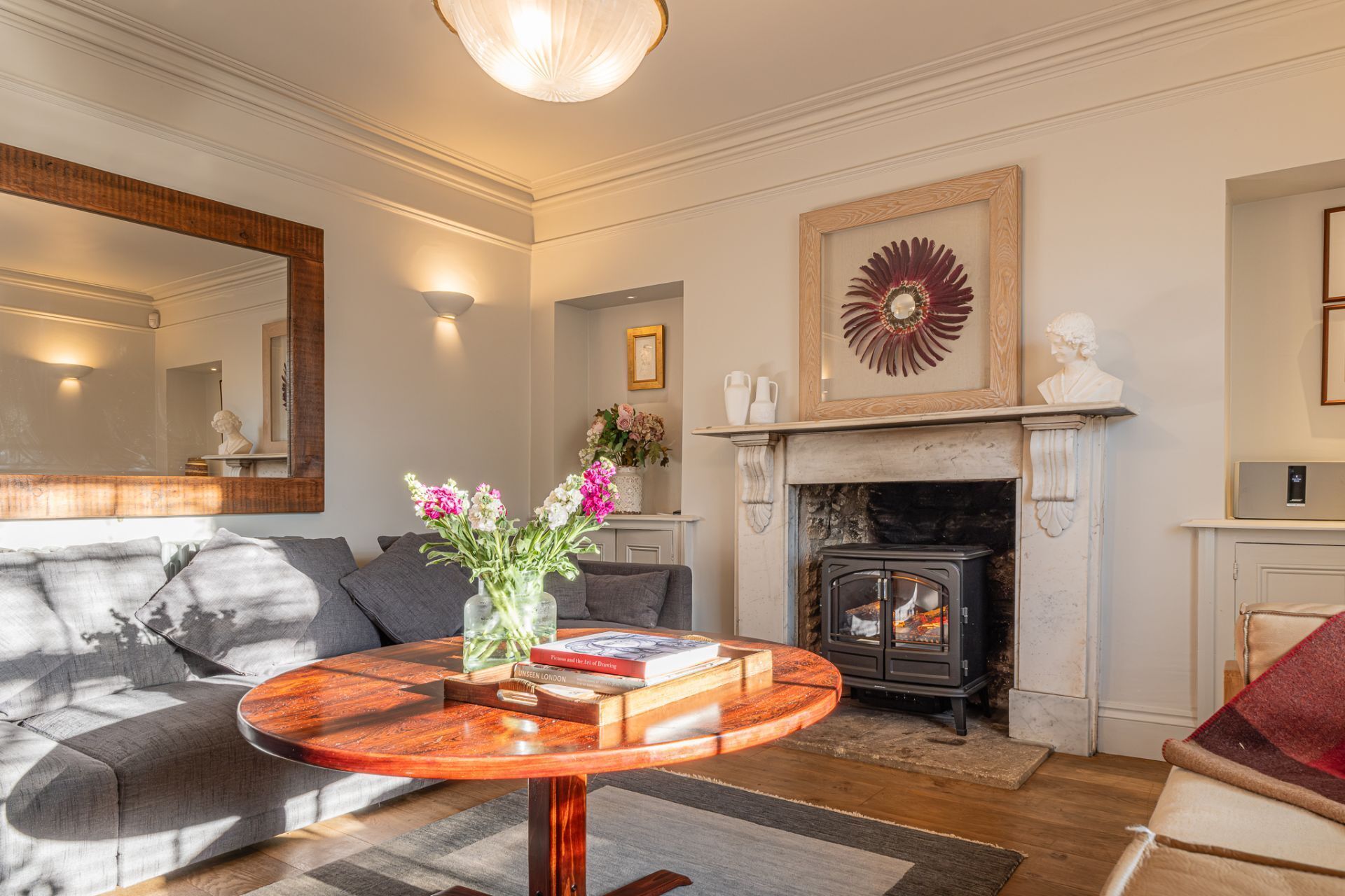 A living room with a fireplace, a round wooden coffee table, a sofa, and a mirror.