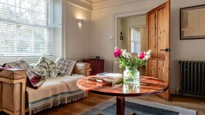 A cozy living room with a sofa, a round wooden coffee table, and a vase of flowers.
