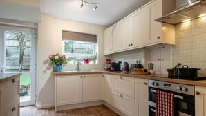 A kitchen with white cabinets, a wooden countertop, a window with a view of greenery, and a red and white checkered towel hanging on the oven.