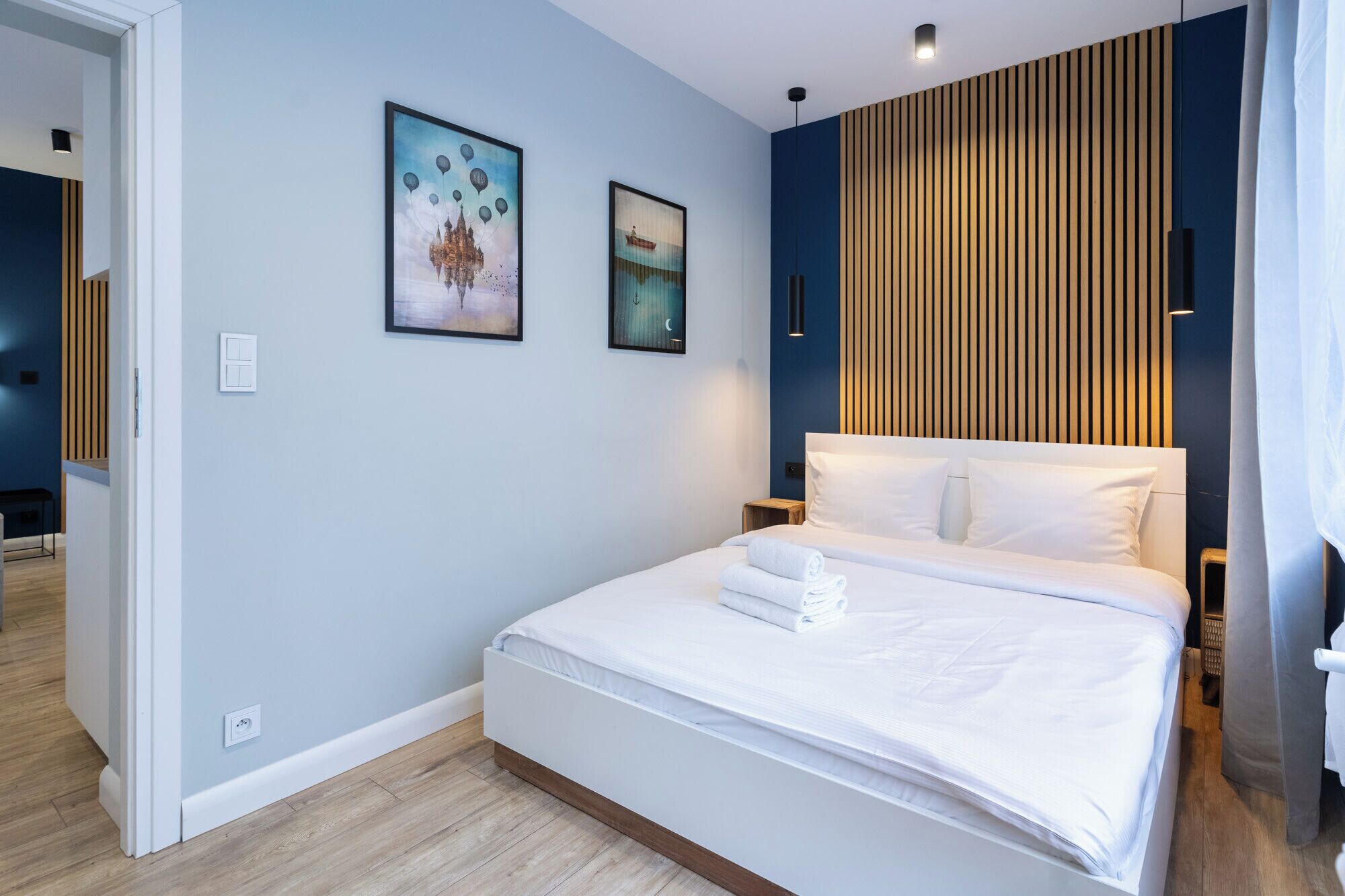 Ein modernes Hotelzimmer mit einem großen Bett, zwei an der Wand befestigten Kunstwerken, einer Wandverkleidung aus Holzleisten und einem weißen Kopfteil.