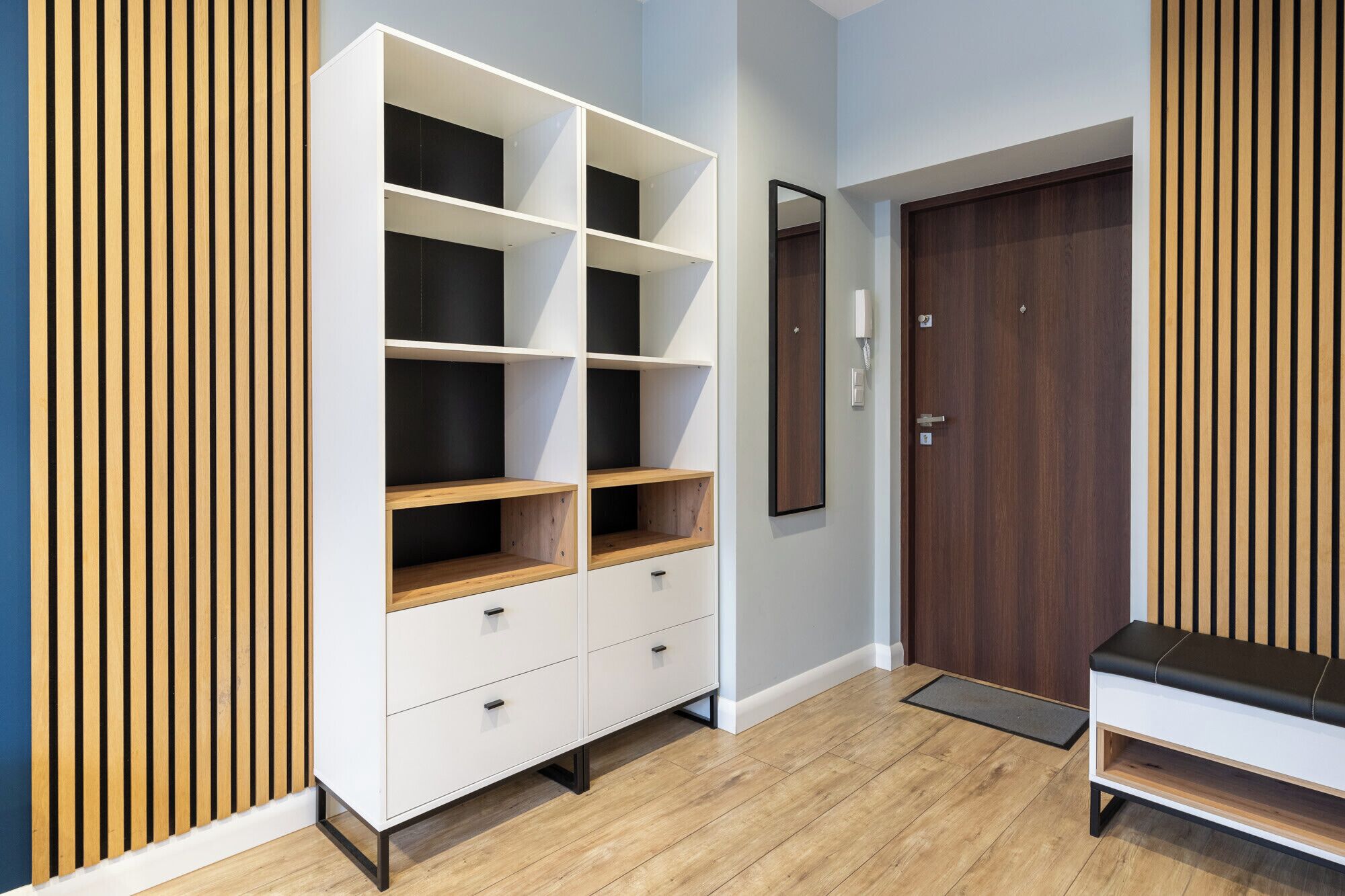Una habitación moderna con un estante blanco, una puerta de madera y un banco.
