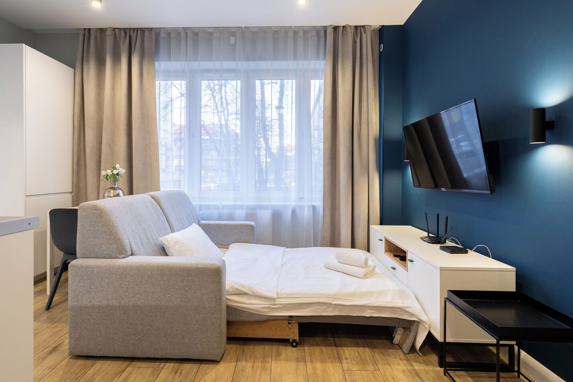 A modern hotel room with a bed, a desk, a chair, and a TV.
