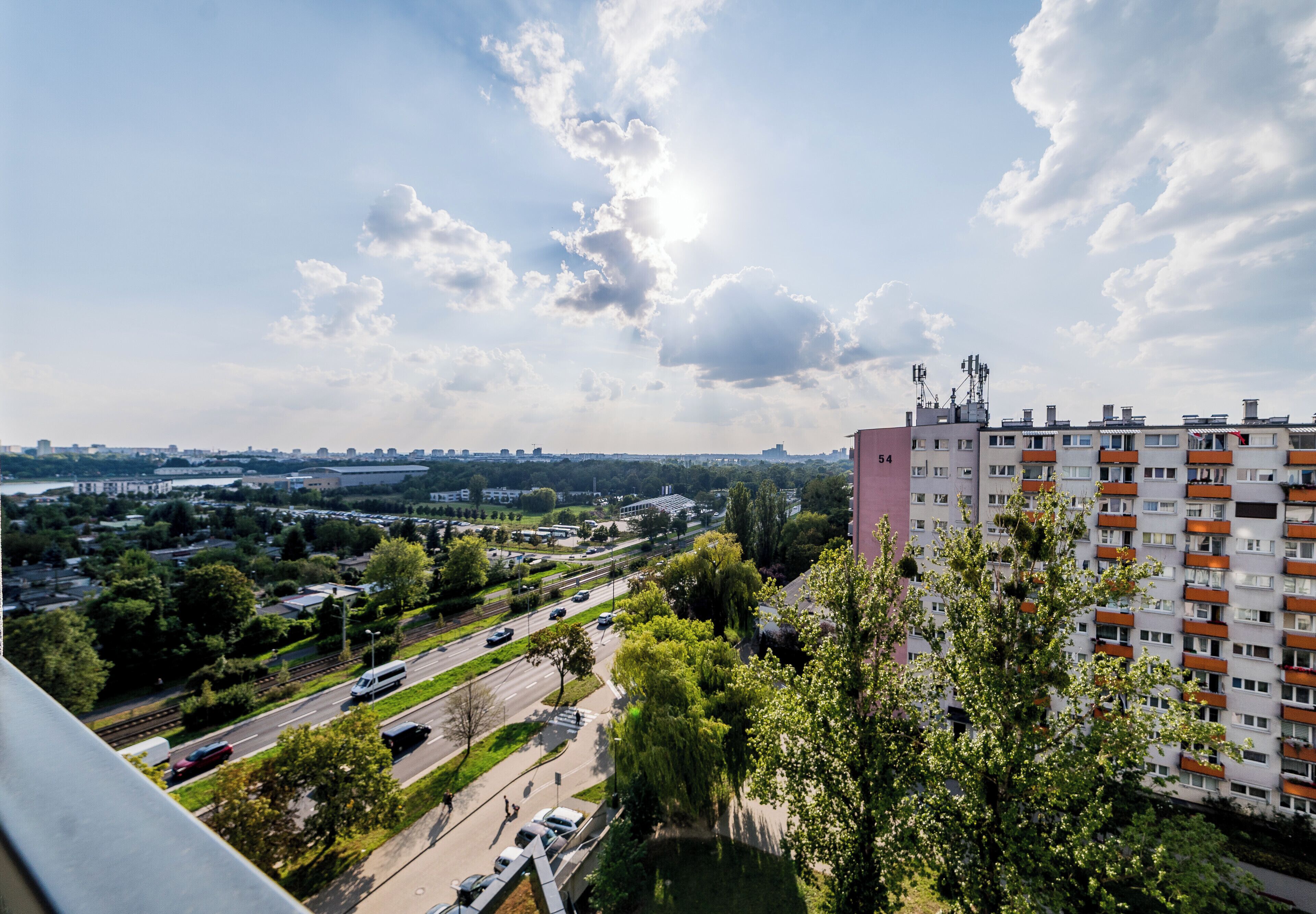 Ein Hochhaus mit mehreren Balkonen, einem Parkplatz und einer Straße mit Fahrzeugen.