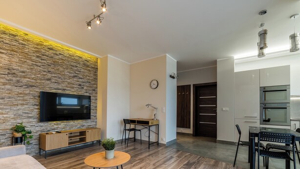 Una sala moderna con pared de piedra, un televisor de pantalla plana, una mesa de centro de madera y un comedor con una mesa y sillas negras.