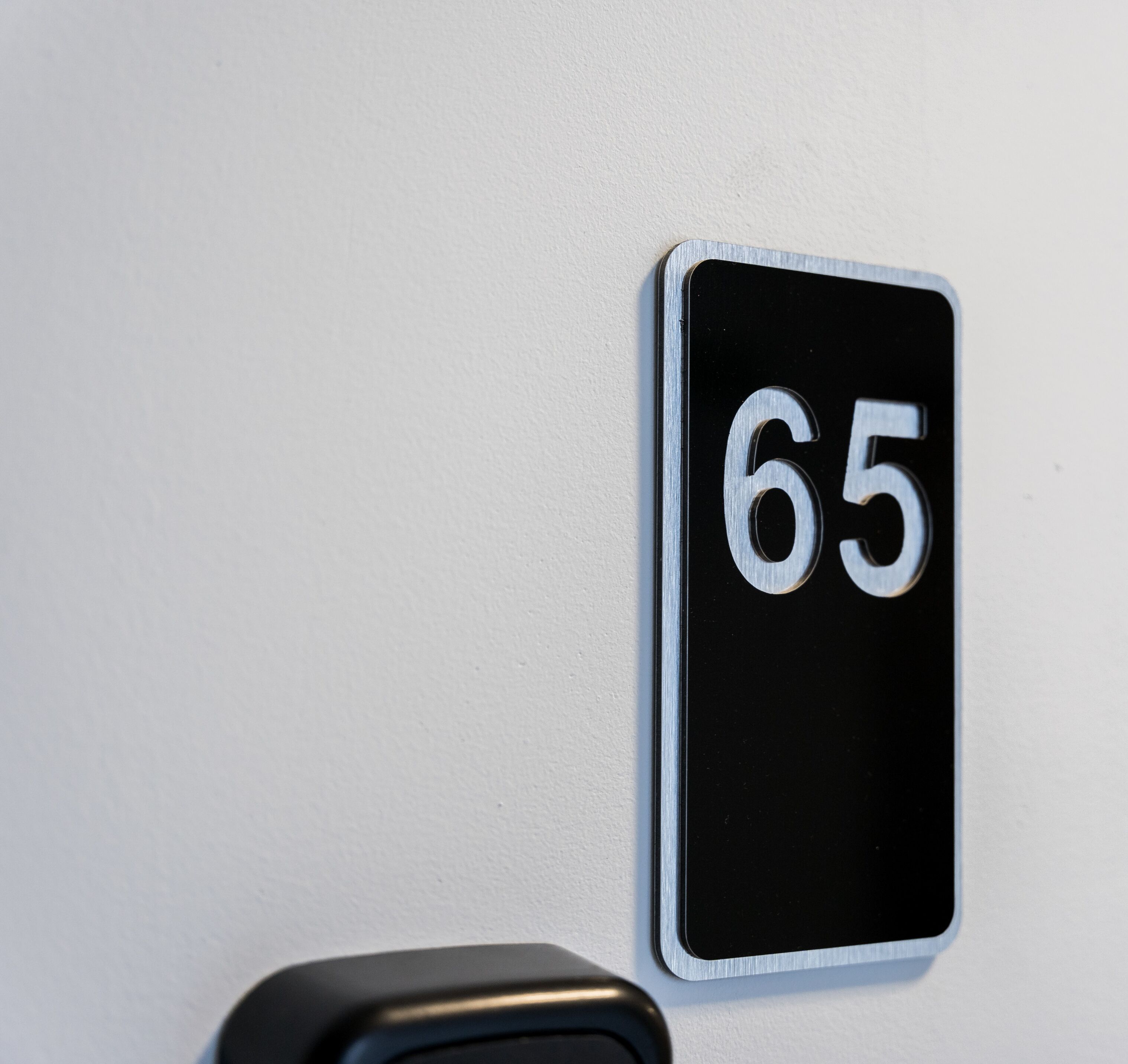 En svartvit skylt med siffran 65 på en vit vägg.