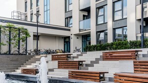 Un edificio moderno con una fuente ornamental en primer plano, escalones que conducen a un balcón y bicicletas estacionadas afuera.
