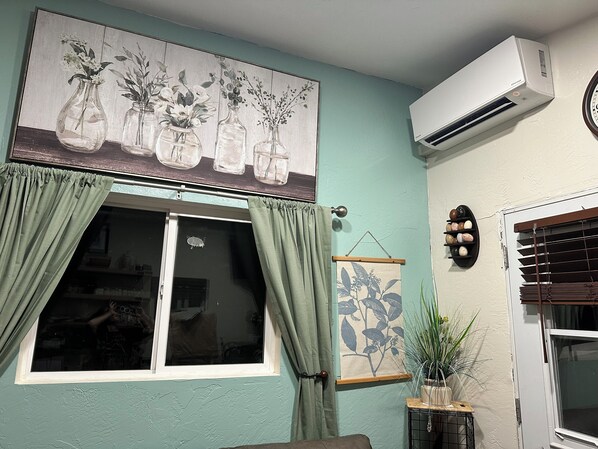 A room with a large window, green curtains, a wall-mounted air conditioner, and a potted plant.