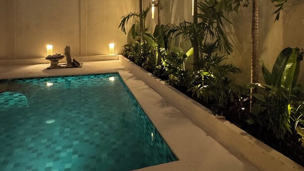 Una piscina con suelo de baldosas, rodeada de exuberante vegetación y una pared.