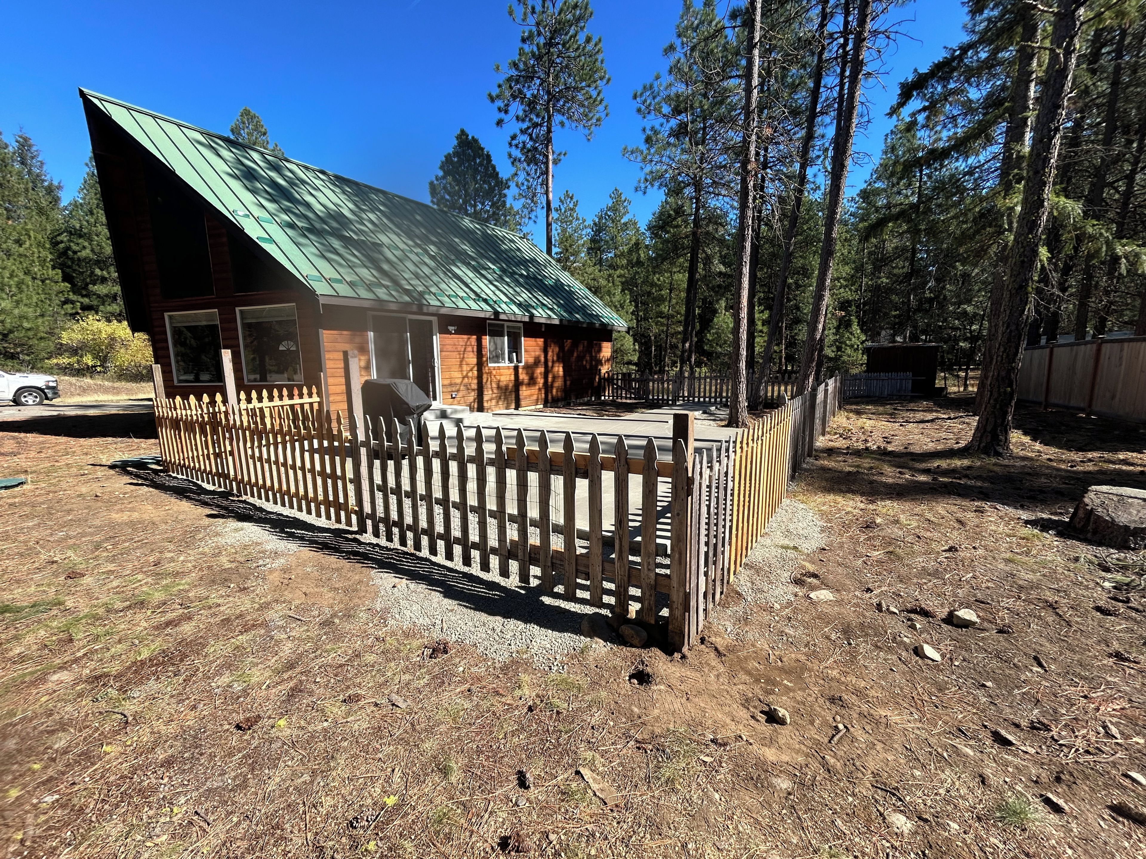 Une cabane avec un toit en pente, entourée d’une clôture en bois, située dans une zone boisée.