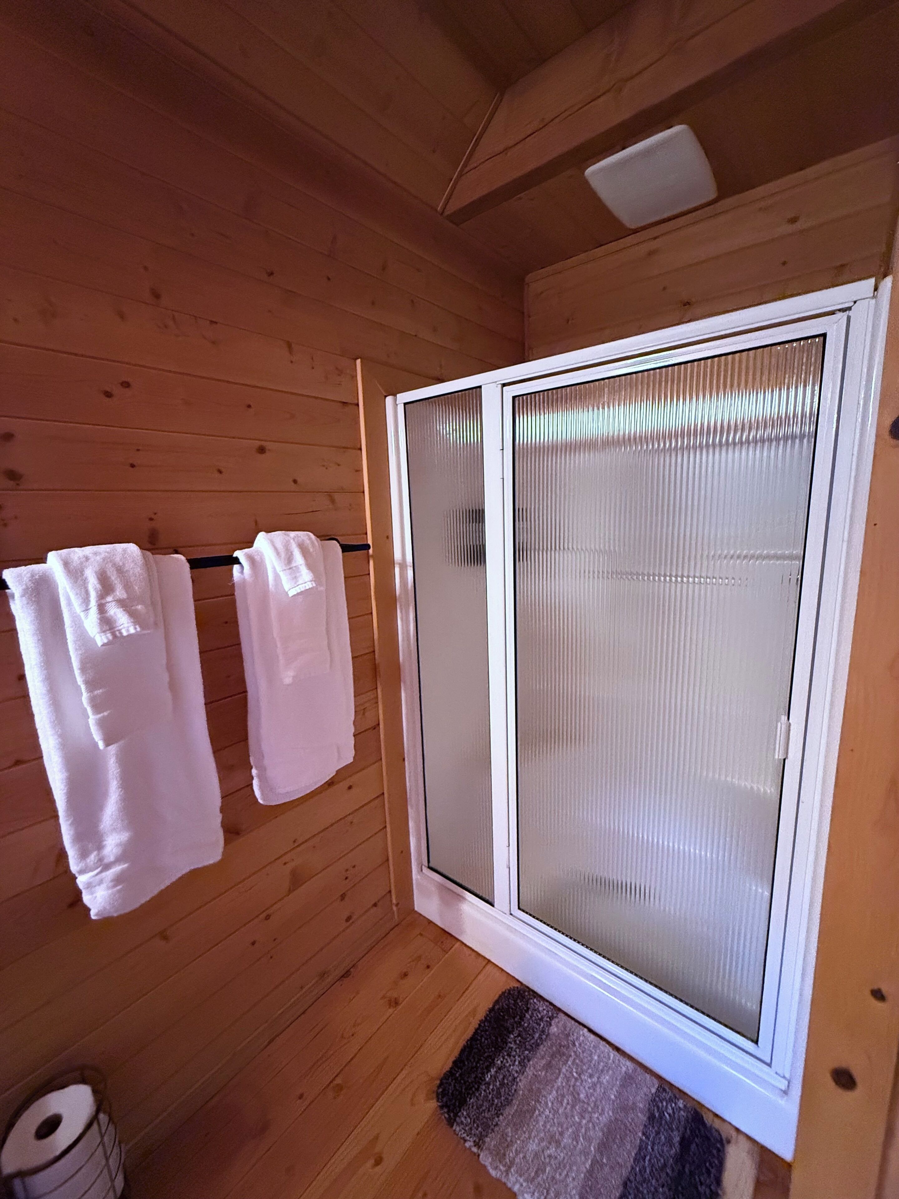 A wooden cabin interior with a sliding glass door, two towels hanging on a rack, and a small rug at the door's base.