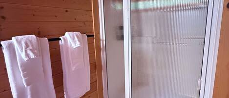 A wooden cabin interior with a sliding glass door, two towels hanging on a rack, and a small rug at the door's base.