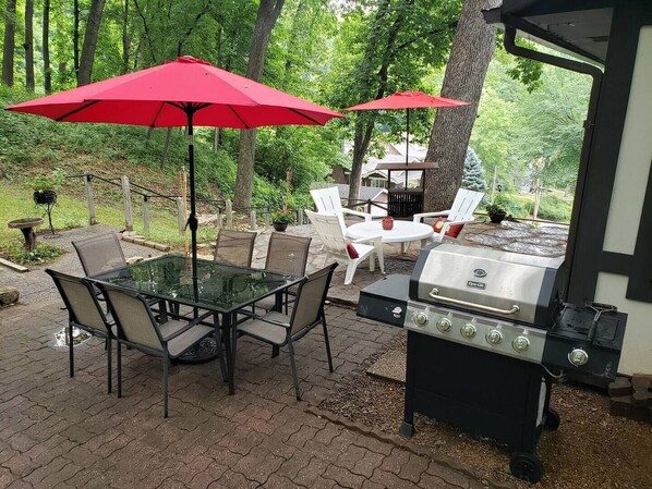 An outdoor patio with a glass table, chairs, and a grill.