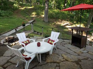 A stone patio with a round table and white chairs, a red umbrella, and a wooden grill structure. - House On the Hill Charming 3-bedroom house with Rec Room, in lovely Savanna (Savanna,)