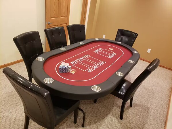 A red poker table surrounded by black chairs in a room with beige carpet and a wooden door.