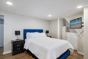 Um quarto com uma cama, duas mesinhas de cabeceira, uma TV fixada na parede e uma escada.