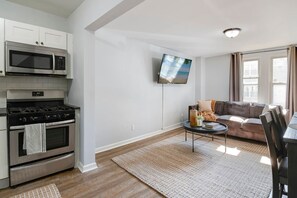 A modern kitchen with stainless steel appliances, a flat-screen TV mounted on the wall, a cozy living area with a sofa and a coffee table, and a wooden floor. - 3 Bedroom Beauty in Bloomfield (Bloomfield)