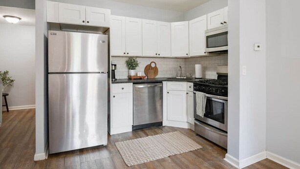 A modern kitchen with white cabinets, stainless steel appliances, a wooden cutting board, and a small potted plant. - 3 Bedroom Beauty in Bloomfield (Bloomfield)