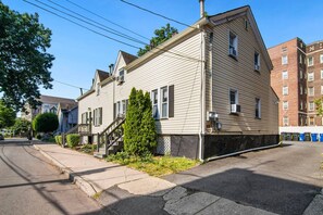 Um edifício residencial de dois andares com varanda frontal, pequeno jardim da frente e garagem.