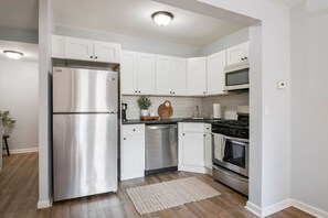 A modern kitchen with white cabinets, stainless steel appliances, a wooden cutting board, and a small potted plant. - 3 Bedroom Beauty in Bloomfield (Bloomfield)