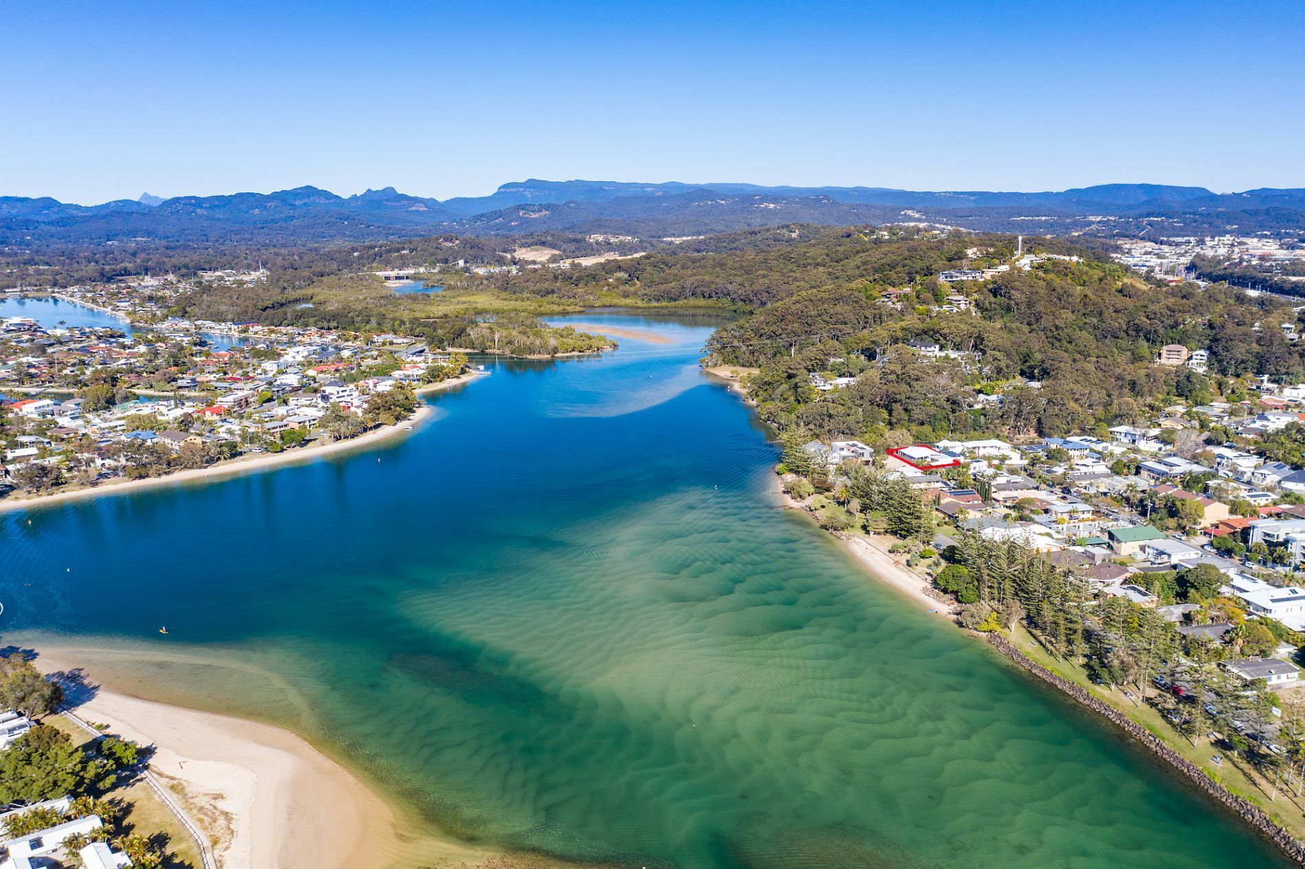 An aerial view of a coastal town with a river, clear waters, and residential areas.
