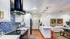 A modern kitchen with white cabinets, blue mosaic backsplash, and wooden flooring. - Cocktails & Cacti | Encanto-Palmcroft Villa | Temp-Controlled Pool + Hot Tub | 4 Suites (Phoenix)