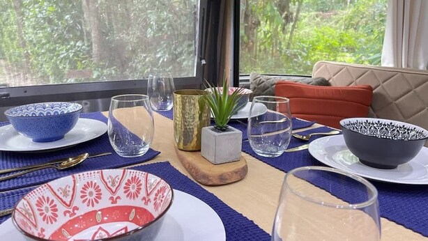 A dining table set with various bowls and glasses, a small plant, and a cushion on a blue mat.