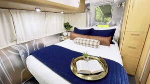 A compact, well-lit interior with a bed, bedside table, and a small window.
