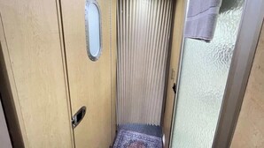 A narrow hallway with a door on the left, a window with blinds on the right, and a small rug on the floor.