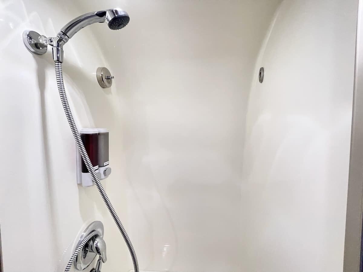 Une cabine de douche blanche et vide, équipée d’un pommeau de douche à main et d’un panneau de commande fixé au mur.
