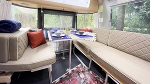 A cozy RV interior with a dining area, cushioned seating, and large windows. - Savannah Home with Modern Airstream, Near Tybee (Savannah)