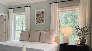 A bedroom with a bed, a nightstand, a lamp, a clock, and a window with curtains. - Savannah Home with Modern Airstream, Near Tybee (Savannah)
