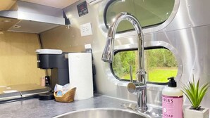 A compact kitchen with a stainless steel sink, a coffee machine, and a window offering a view of greenery. - Savannah Home with Modern Airstream, Near Tybee (Savannah)