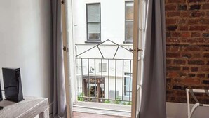 Ein Zimmer mit Holzboden, einem Korbtisch und Blick durch eine Tür auf einen Balkon mit Metallgeländer.