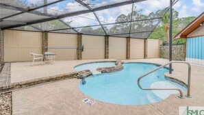 A covered outdoor swimming pool with a table and chairs, surrounded by a stone wall and a covered area with a metal roof. - Poolside Family Haven Near Beach w/ Game Room (Savannah)