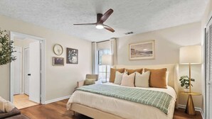 A bedroom with a bed, a ceiling fan, a bedside table with a lamp, and a window. - Dog-Friendly Savannah Cottage Near Tybee (Savannah)
