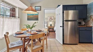 A compact kitchen with a stainless steel refrigerator, a dining area with a table and chairs, and a view through an open door to a bedroom. - Dog-Friendly Savannah Cottage Near Tybee (Savannah)