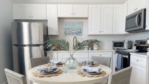 A modern kitchen with white cabinets, stainless steel appliances, a round dining table with placemats, and wicker chairs. - Modern Duplex 3 Blocks from Forsyth Park (Savannah)