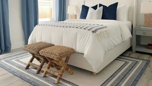 A bedroom with a bed, two bedside tables, a window with curtains, a wall-mounted picture, and a woven bench. - Modern Duplex 3 Blocks from Forsyth Park (Savannah)