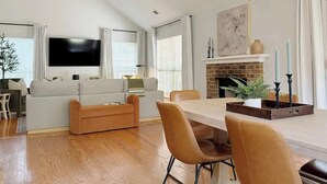 Una sala de estar moderna con un sofá, una mesa de comedor con sillas, un televisor montado en la pared y una chimenea con velas.