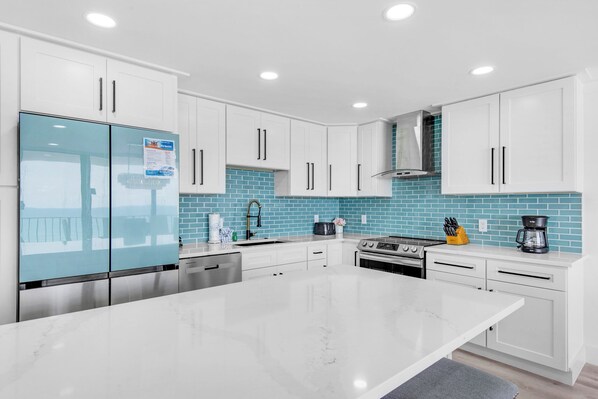 A modern kitchen with white cabinets, a large island, and a blue-tiled backsplash.