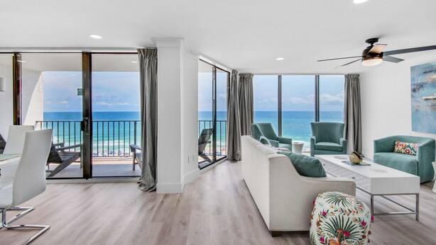 A modern living room with a balcony overlooking the ocean, furnished with a sofa, chairs, and a coffee table.